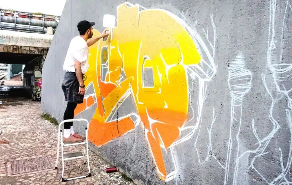 Street artist working on colored graffiti at public wall
